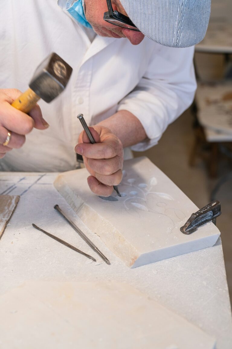 Handen van een beeldhouwer bewerken wit marmer met hamer en beitel